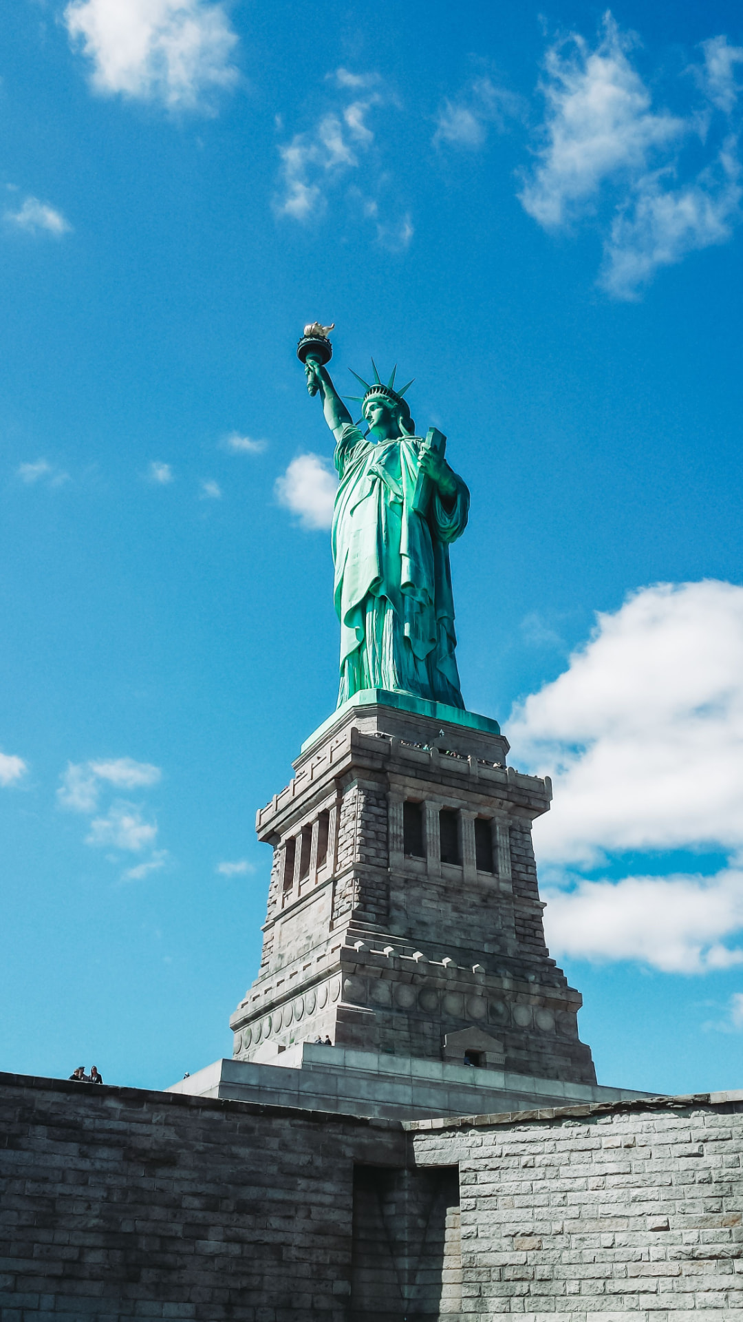 The Statue of Liberty against a bright sky with scattered clouds
