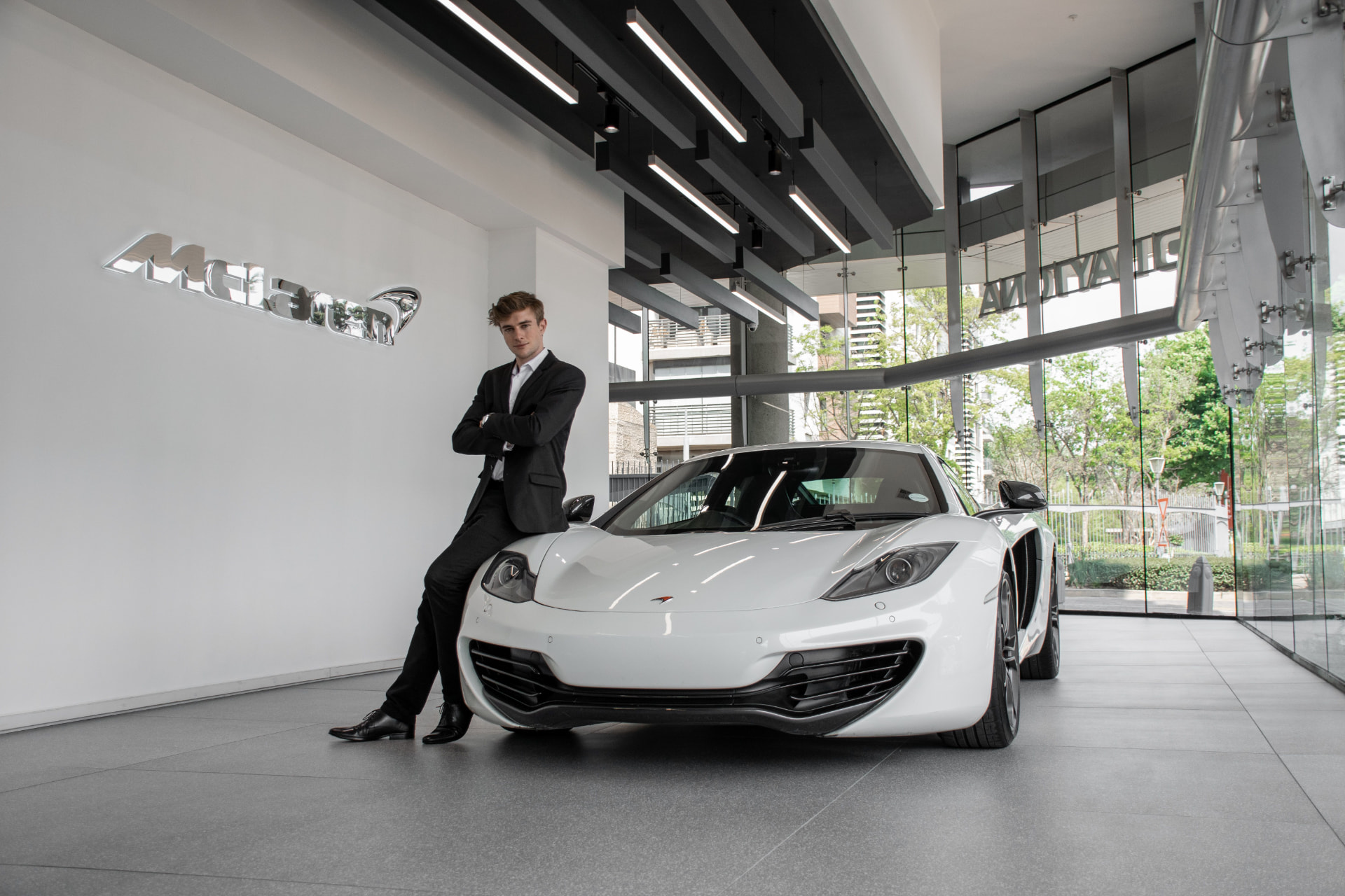 An owner leaning on a white sports car in a bright showroom